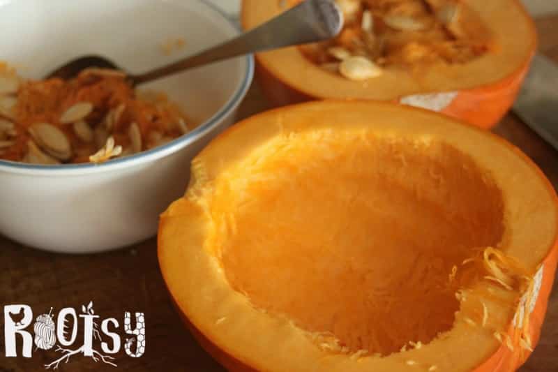 A pumpkin half with the seeds removed sitting next to a bowl of the seeds with a spoon.