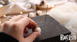 Fingers squeezing felted wool ball into acorn cap.