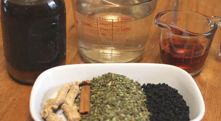 herbs in white bowl with jars of honey, brandy, and distilled water for making elderberry cordial