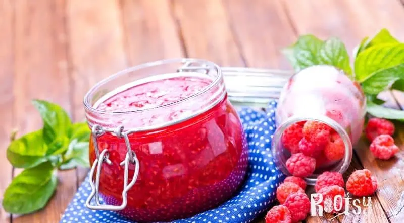image of homemade raspberry in canning jars with fresh raspberries on a blue and white towel