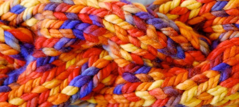 A close-up of colorful, chunky yarn in a twisted pattern perfect for fall crafts. The vibrant shades of red, orange, yellow, purple, and blue create a visually rich and textured appearance that embodies the essence of autumn creativity.