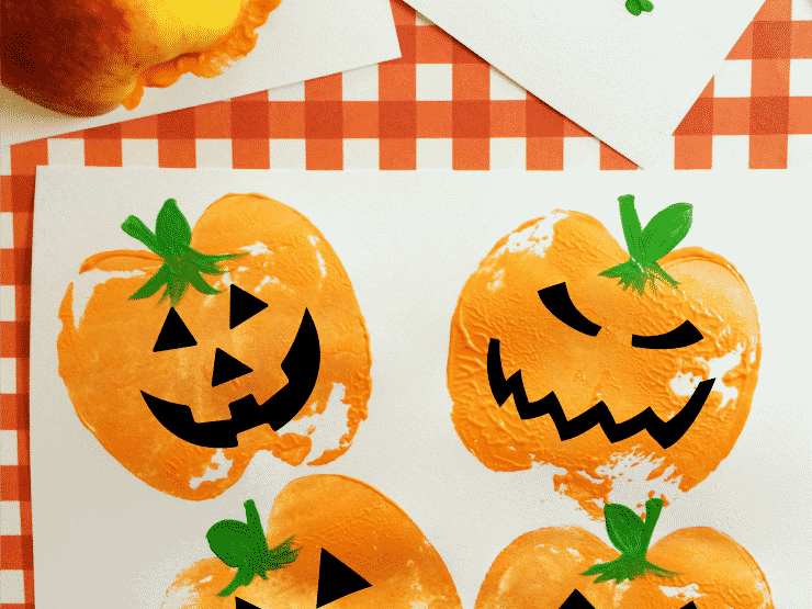 A delightful fall craft project features pumpkin stamps with various jack-o'-lantern faces, painted in vibrant orange on white paper. The papers elegantly rest on a classic red and white checkered surface, capturing the essence of autumn creativity.