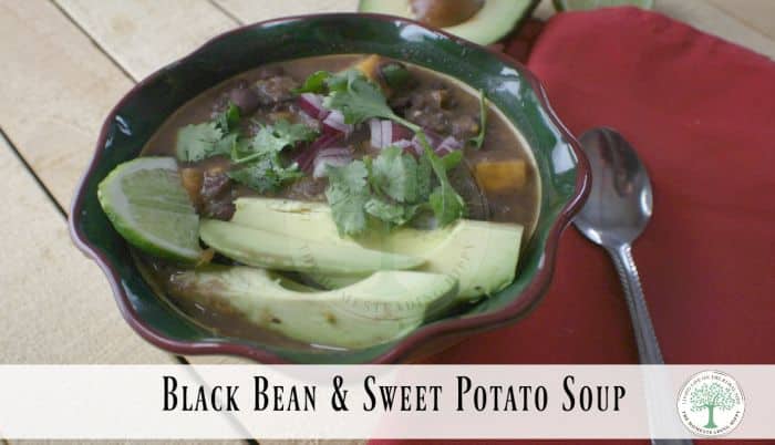 A bowl of black bean and sweet potato soup garnished with sliced avocado, lime wedges, cilantro, and diced red onion. A spoon rests nearby on a red napkin. Text on the image reads "Black Bean & Sweet Potato Soup.