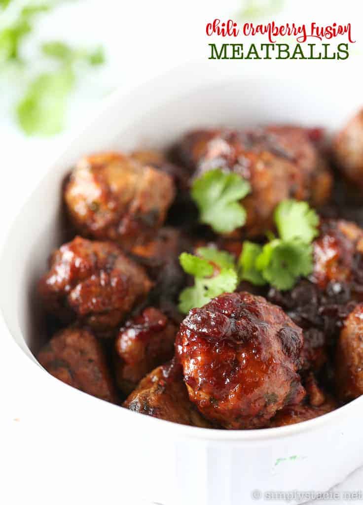 A dish of chili cranberry fusion meatballs garnished with cilantro. The meatballs are glazed and served in a white bowl, with some herbs visible in the background.