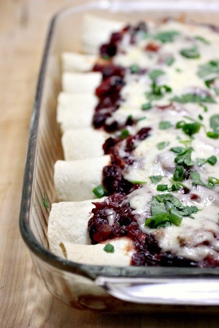 A glass baking dish filled with freshly baked enchiladas, topped with melted cheese and garnished with chopped cilantro. The enchiladas have a rich, red sauce spread over them.