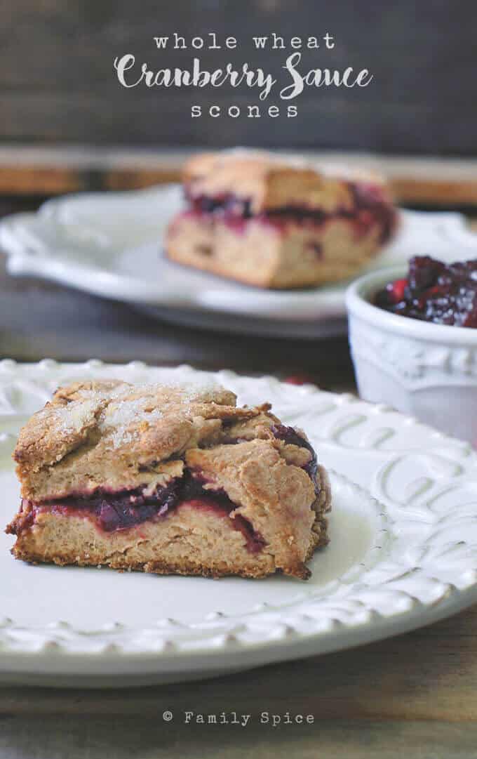 A whole wheat scone filled with cranberry sauce on a white plate, with more scones and cranberry sauce in a bowl in the background. The text above reads "whole wheat Cranberry Sauce scones.