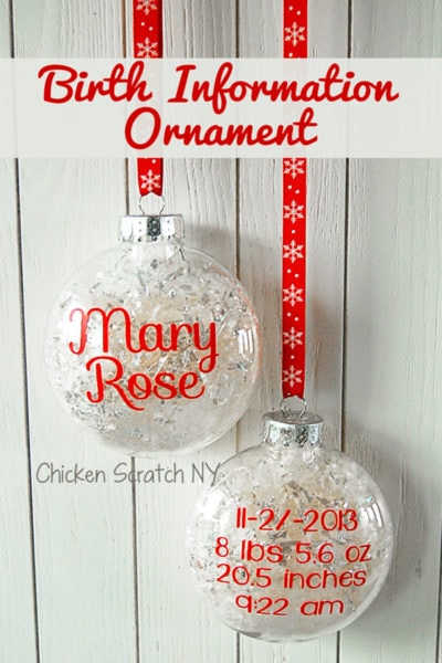 Two clear ornaments hang against a white wooden background on red snowflake ribbons. One reads "Mary Rose," and the other displays "11-2-2013, 8 lbs 5.6 oz, 20.5 inches, 9:22 am." Text above says "Birth Information Ornament.