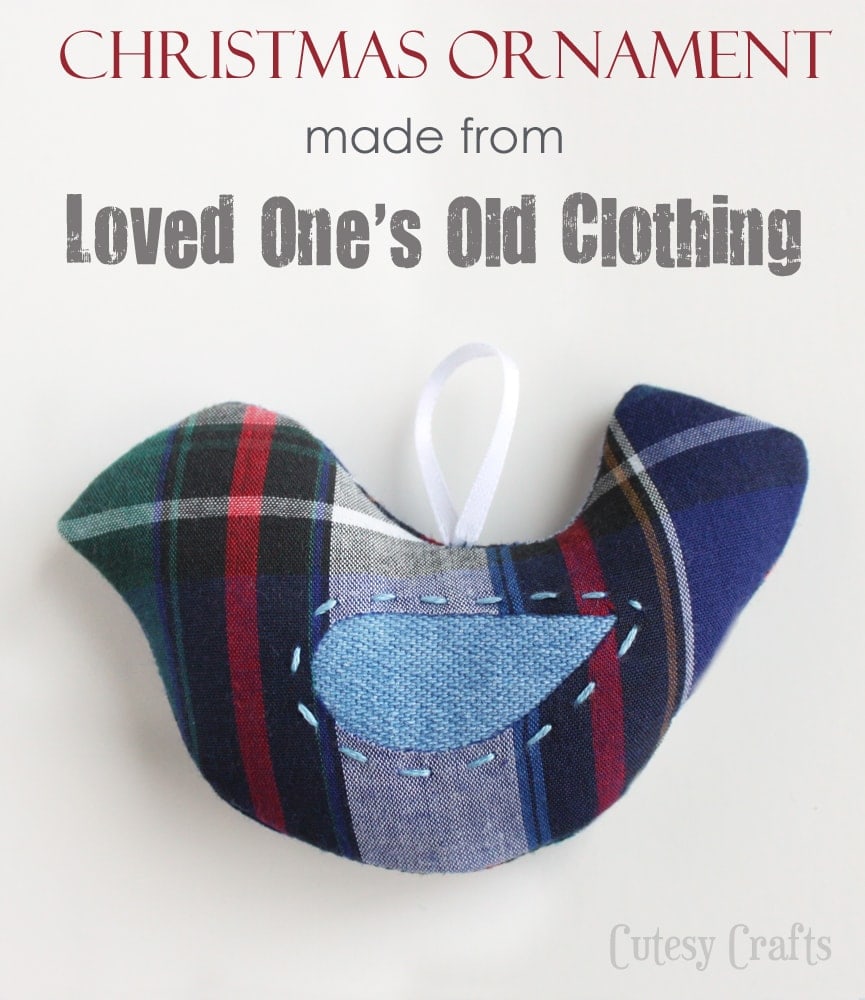 A handmade bird-shaped Christmas ornament crafted from plaid fabric, embellished with a blue patch and white ribbon loop for hanging. Text reads "Christmas ornament made from loved one's old clothing" with the "Cutesy Crafts" logo.