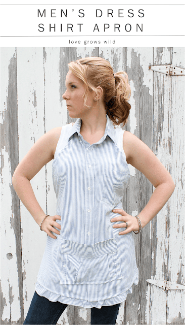 A person wearing an apron made from a striped men's dress shirt stands in front of a weathered wooden wall. The sleeveless apron has a collared neckline and button details. The person has their hands on their hips and is looking to the side.