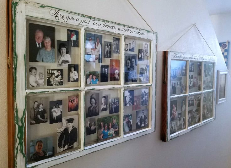 Old window frames repurposed as picture frames hang on a wall, displaying a collage of various black and white and color family photos. The frames have handwritten phrases on them, adding a nostalgic and personal touch to the decor.