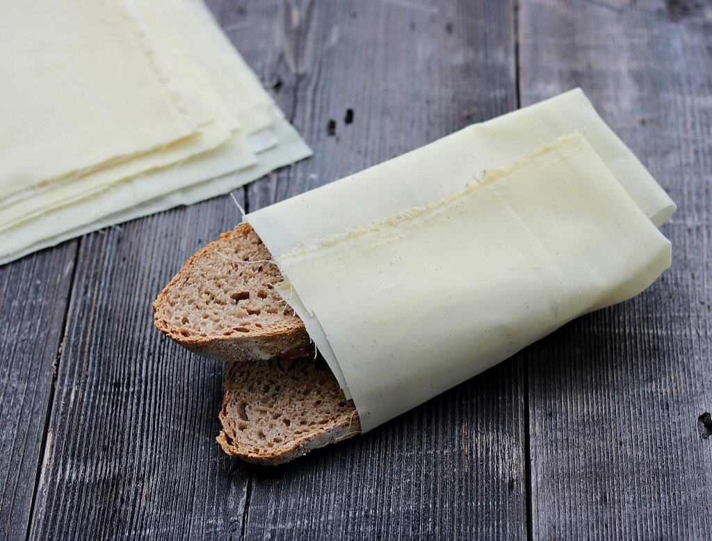 A loaf of bread wrapped in thin sheets of cheese, placed on a rustic wooden surface. Additional cheese sheets are stacked in the background.