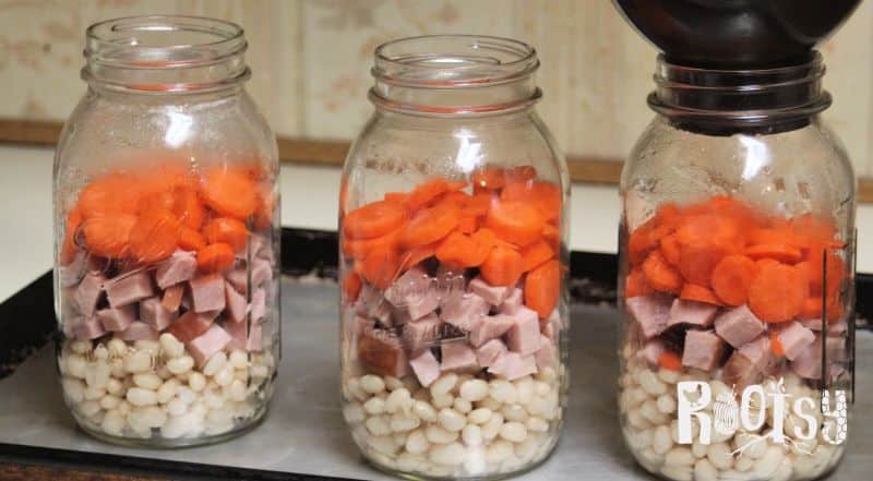 3 quart jars being filled with navy beans, ham, and carrots. 