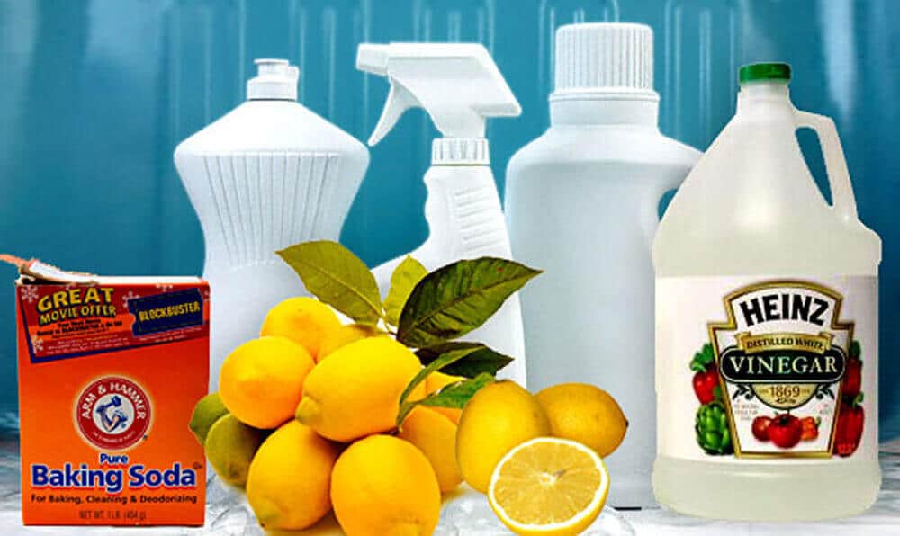 A money-saving collection of cleaning products includes bottles of spray and liquid, a box of Arm & Hammer baking soda, Heinz vinegar, and fresh lemons—one cut in half—all set against a blue background. Perfect for keeping your bathroom sparkling without breaking the bank.