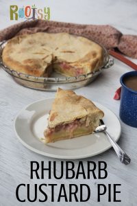 A slice of rhubarb custard pie on a white plate with a fork sitting in front of a whole pie and blue tin cup of coffee.