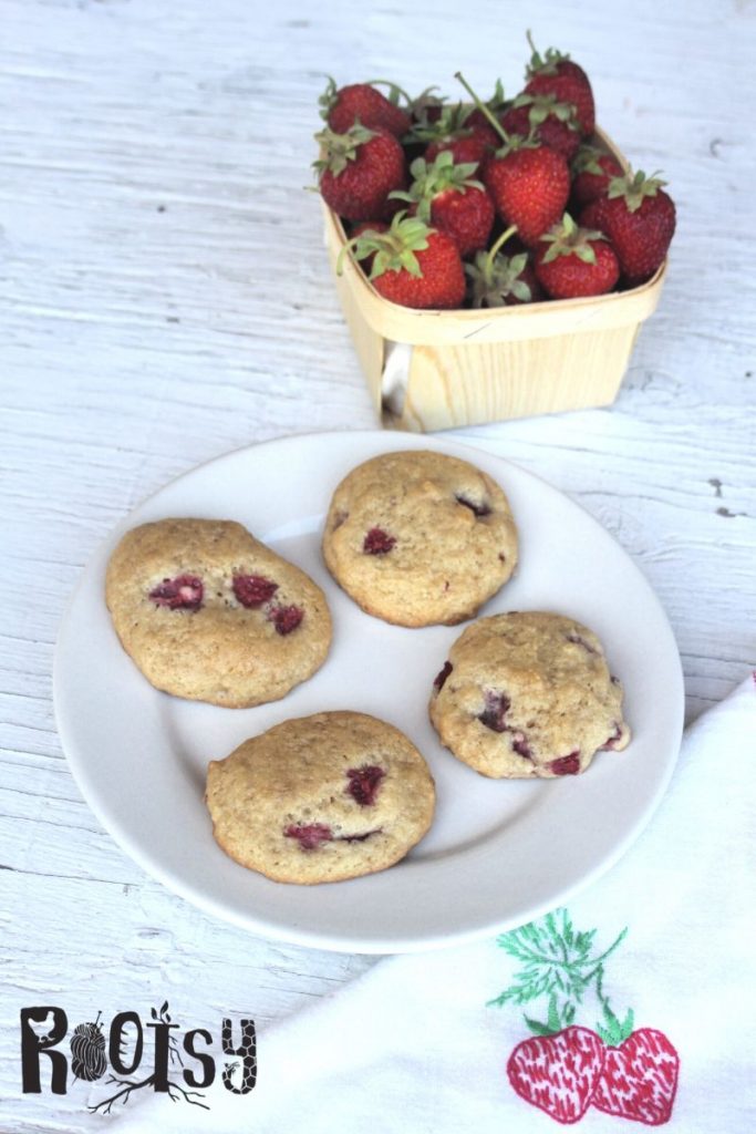 Fruit cookies on a plate with a napkin and basket of fresh strawberries.