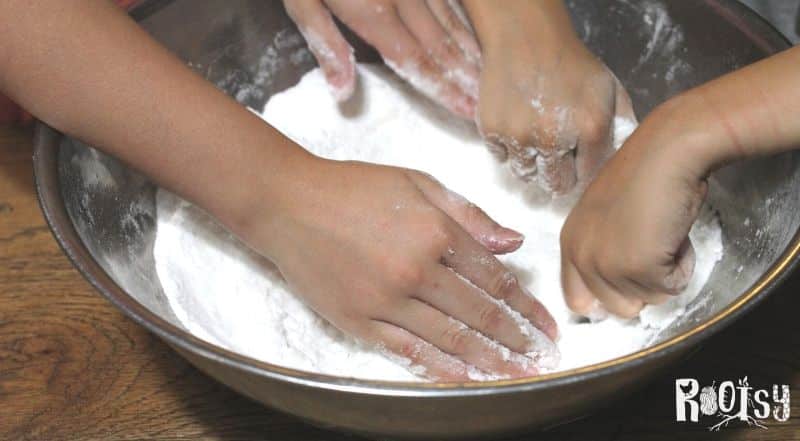 two pairs of children's hands mixing bath bomb mixture in large metal bowl