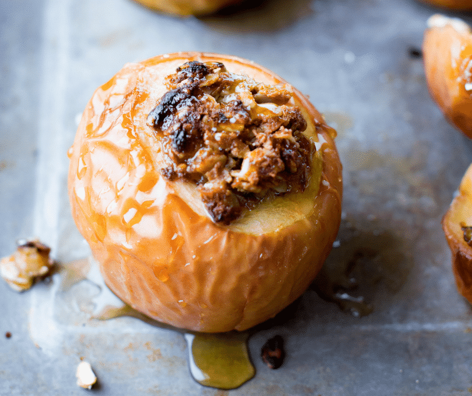Close-up of a baked apple, showcasing one of the delightful apple recipes, filled with a spiced nut and oat mixture, drizzled with honey. The apple is golden brown and lightly caramelized, sitting on a baking sheet.