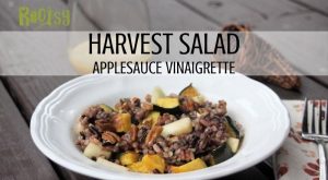 A white bowl full of harvest salad with a napkin and fork to the right, a small pitcher of dressing behind it with a wicker cornucopia and text overlay stating: harvest salad applesauce vinaigrette.