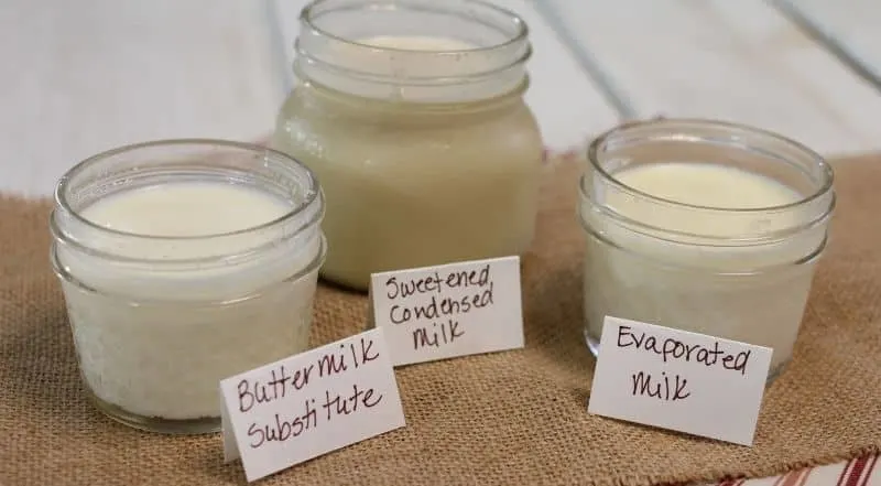 3 jars of milk products lined up on a piece of burlap with tags labeling them in front stating: buttermilk substitute, sweetened condensed milk, evaporated milk.
