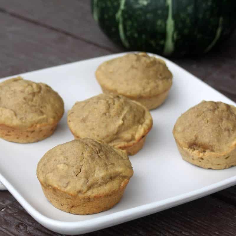 Five pumpkin lentil muffins rest on a white square plate, with a green pumpkin in the background on a wooden surface.