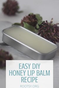 Honey lip balm in a rectangular metal tin surrounded by dried flowers on white table with text overlay reading: easy DIY honey lip balm recipe.