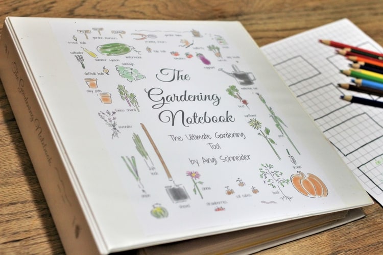 A gardening notebook lies on a wooden table with a freshly sharpened set of colored pencils and graph paper beside it. The cover, reminiscent of classic gardening books, showcases colorful illustrations of tools and plants, and the title reads "The Gardening Notebook.