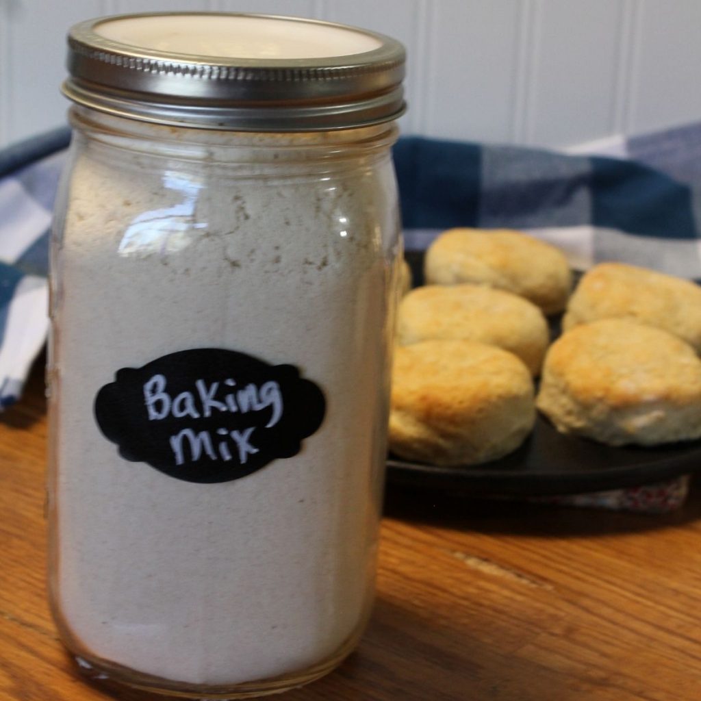 A sealed jar filled with baking mix and labeled with words 'baking mix' with cast iron skillet full of biscuits in the background.