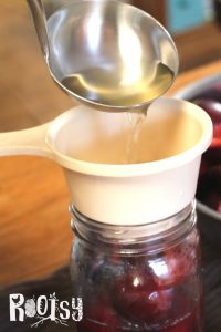 ladling syrup into canning jar with plum halves
