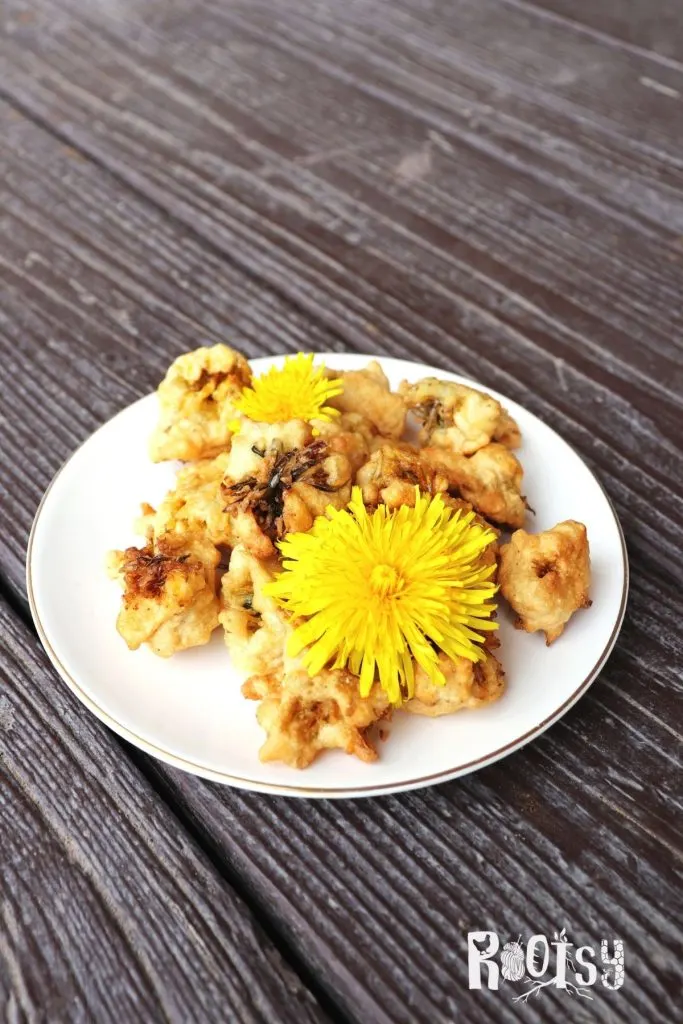 A plate stacked with cooked fritters with 2 dandelion flowers in front.