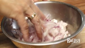 red onion slices in metal bowl being massaged with salt for fermenting