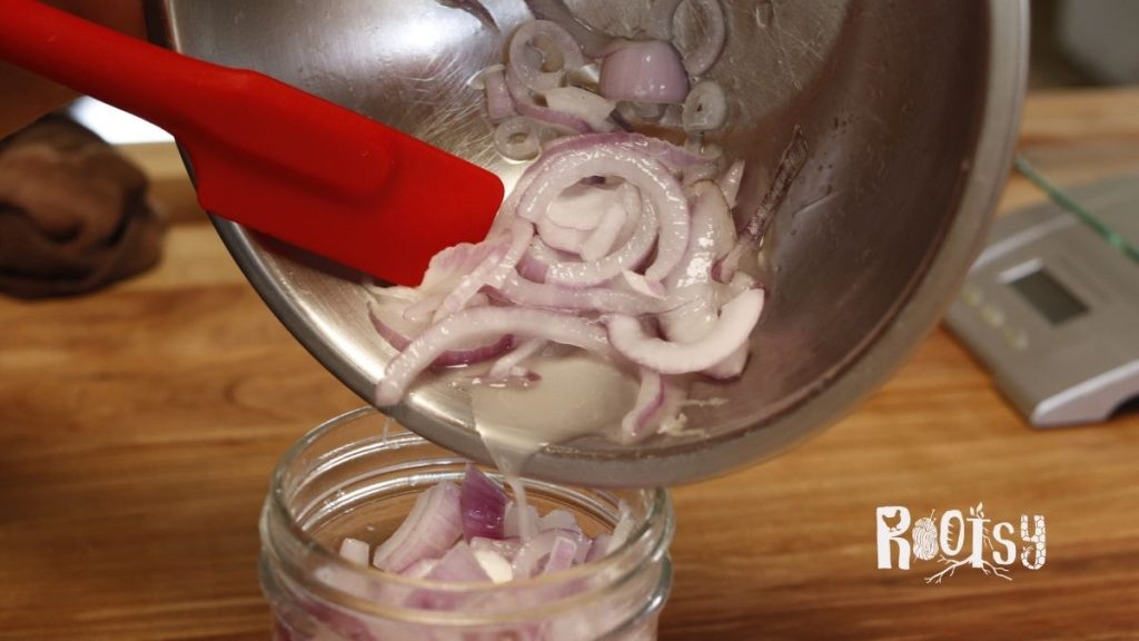 fermented red onions being poured from metal bowl into mason jar