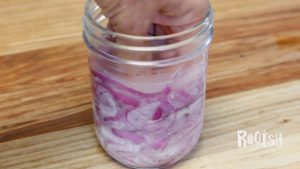 red onion slices in a saltwater brine being pushed down in mason jar