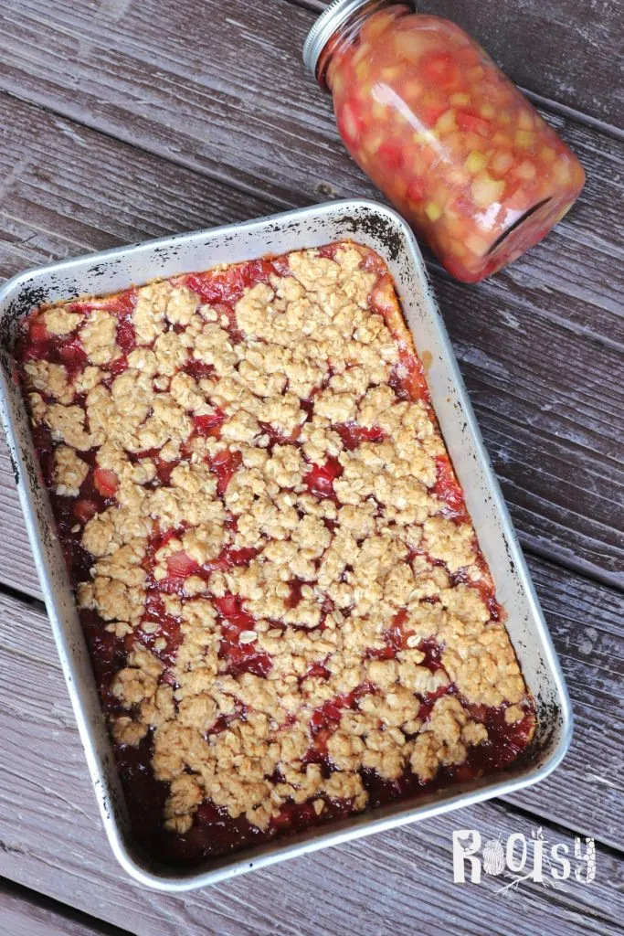 A full pan of rhubarb oatmeal bars as seen from above with a glass jar of rhubarb pie filling sitting next to it.