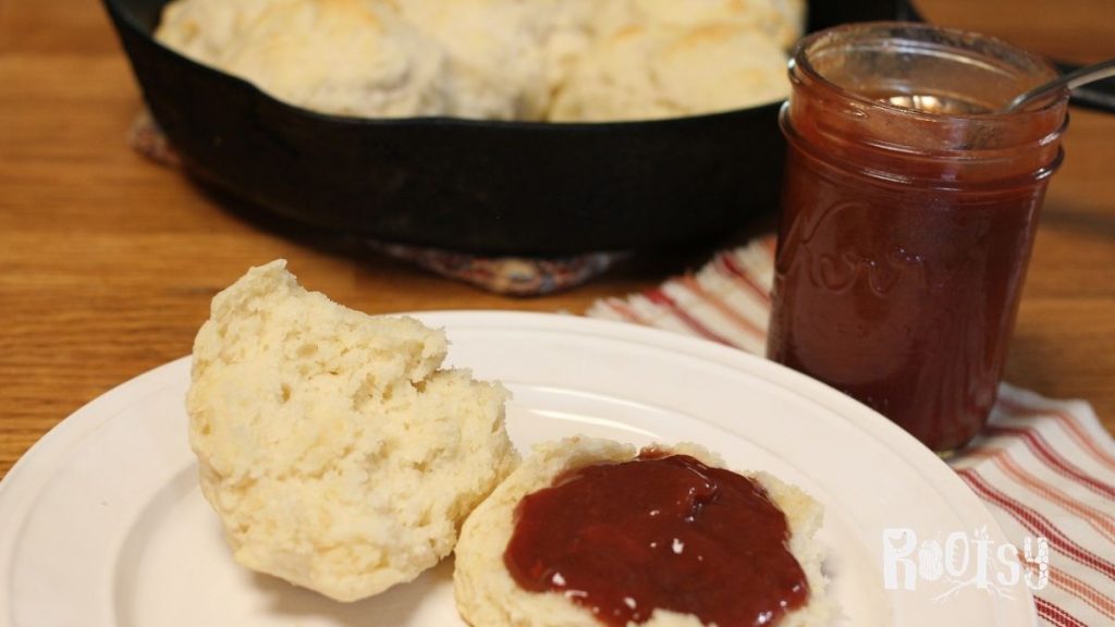 home canned plum butter on a biscuit with a cast iron skillet of biscuits in the background