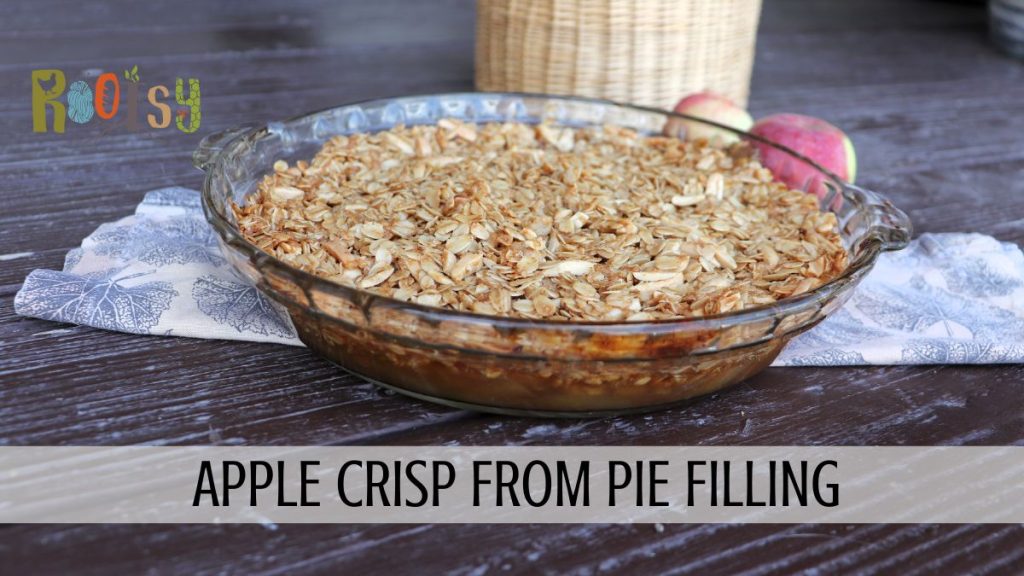 An apple crisp sits on a leaf patterned cloth with fresh apples and a basket in the background. A text overlay reads: apple crisp from pie filling.