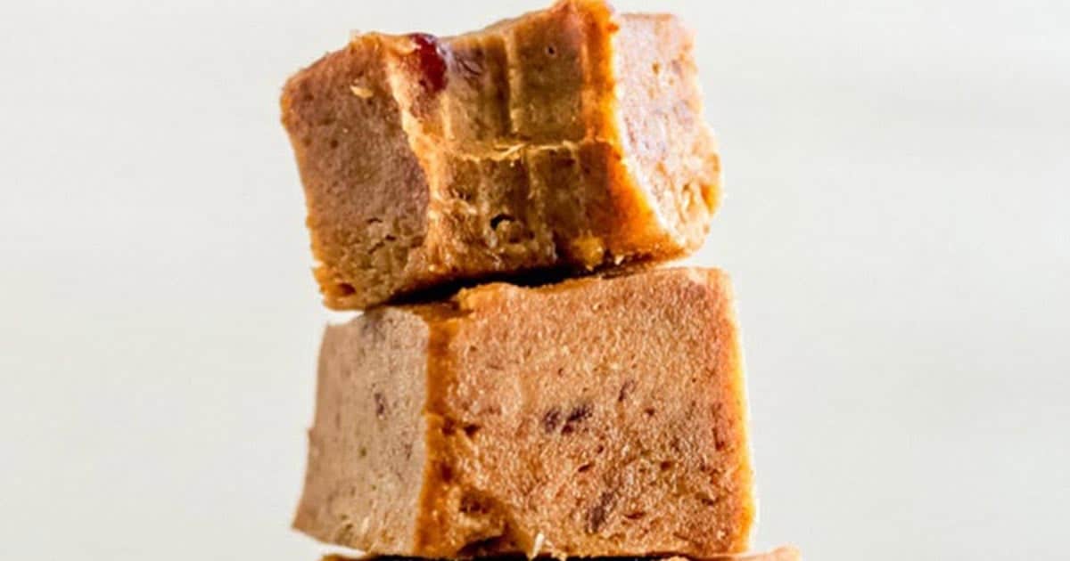 Close-up of three stacked pieces of creamy brown pumpkin fudge against a light background. The fudge appears rich and smooth, with a few visible nut or spice flecks throughout—perfect for autumn dessert recipes.