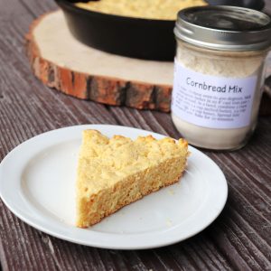 A slice of cornbread on a plate with a jar of cornbread mix in the background.