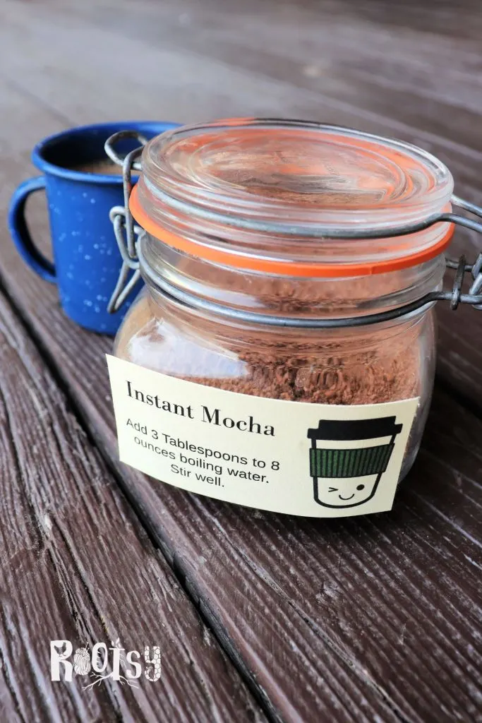 A jar labeled instant mocha sits on a table with a blue tin coffee cup behind it.