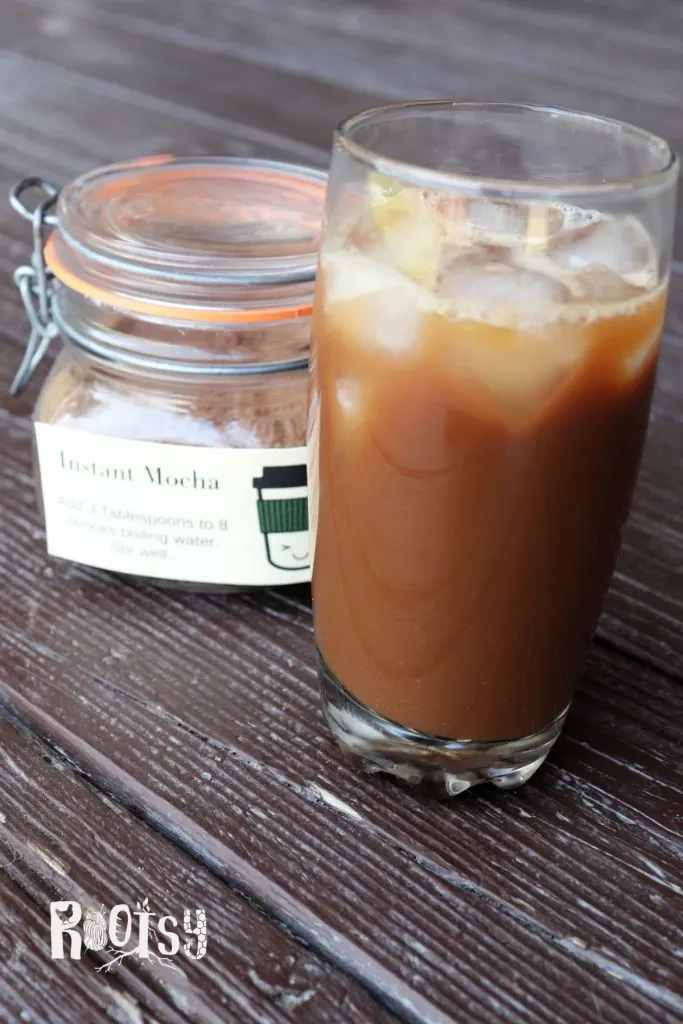 A glass with ice and brown liquid sits on a table with a jar labeled instant mocha behind it.