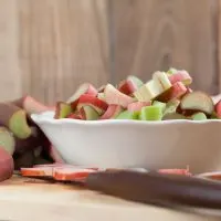 white bowl of chopped rhubarb on wooden counter