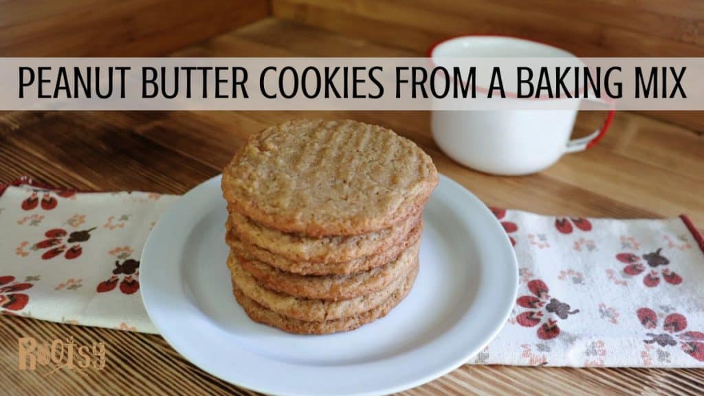 A stack of peanut butter cookies sits on a white plate with a floral-patterned napkin nearby and a white mug with a red rim in the background. Text across the image reads “Peanut Butter Cookies From A Baking Mix.”.