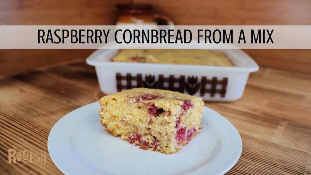 A slice of raspberry cornbread sits on a white plate in the foreground, with a larger dish of the same cornbread in a white baking pan behind it. Text across the image reads "Raspberry Cornbread from a Mix.