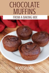 A white plate with four chocolate muffins is on a wooden surface, with a red cloth in the background. Text above the plate reads: "Chocolate Muffins from a Baking Mix. rootsy.org.