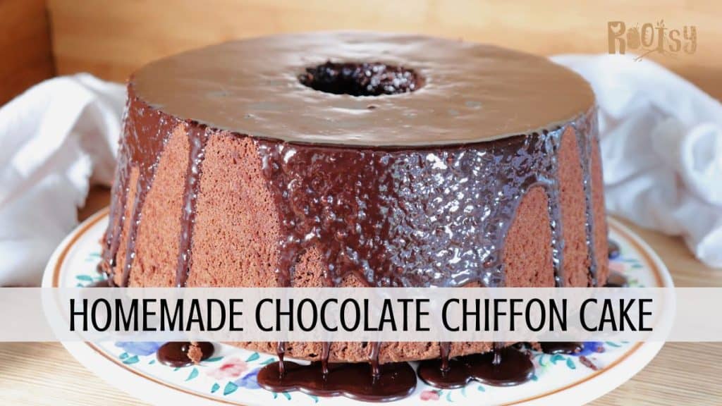 A round chocolate chiffon cake with chocolate glaze dripping down the sides sits on a floral plate. A white cloth is in the background, and text reads “Homemade Chocolate Chiffon Cake.”.