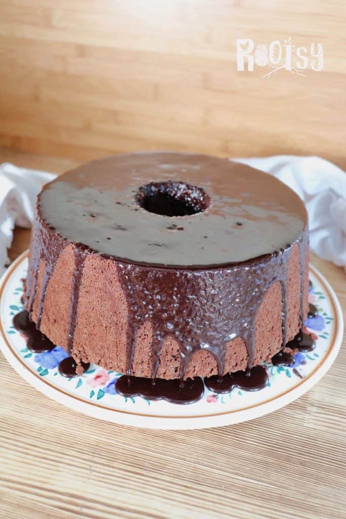 Chocolate chiffon cake with a shiny chocolate glaze dripping down the sides, displayed on a floral-patterned plate against a wooden background.